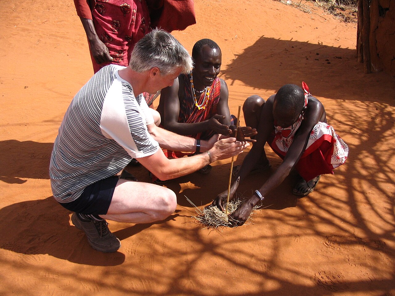 A Maasai host and a traveler share a cultural activity in a Kenyan village
